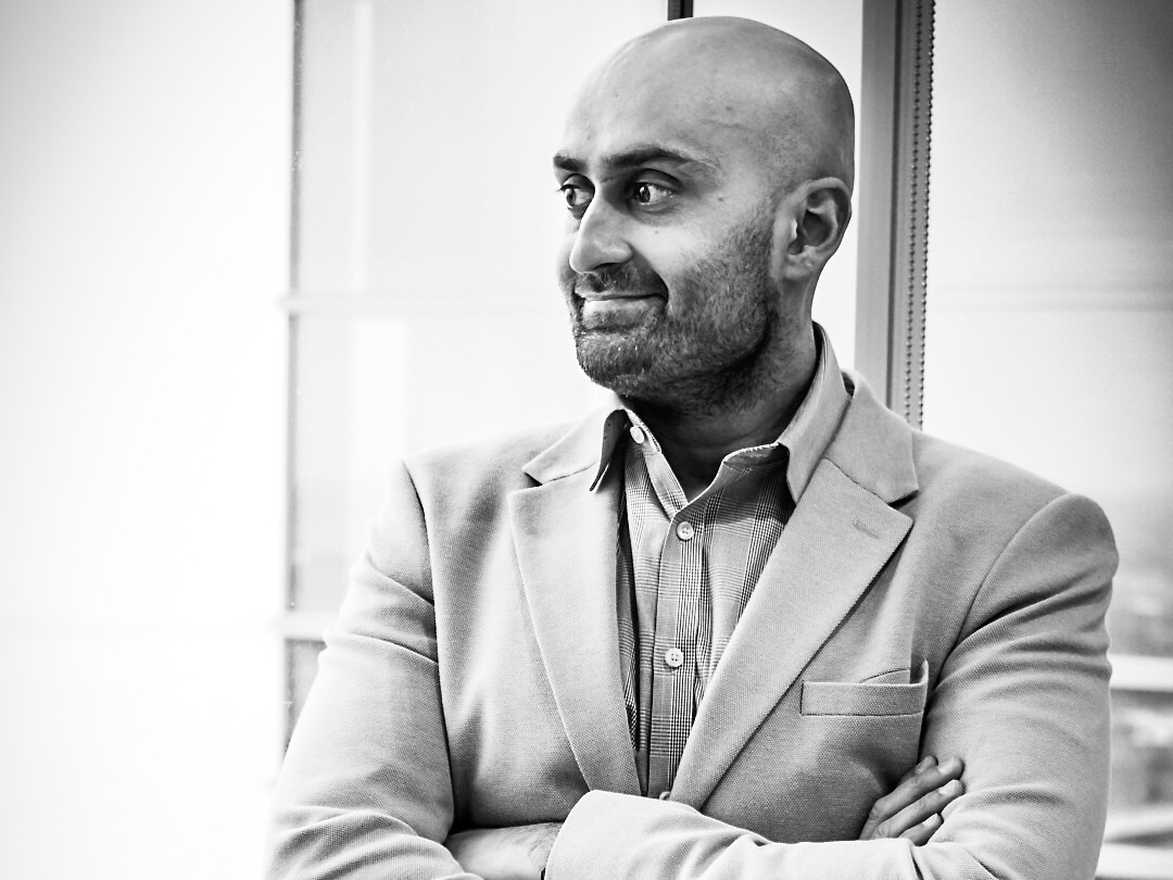 Black-and-white headshot of Ahmed Azam, looking to the side, arms crossed