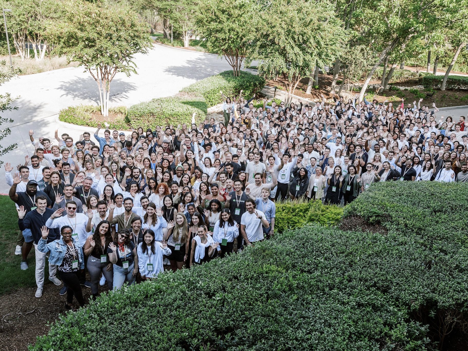 A huge crowd of Headway employees wave and smile in a group photo on the lawn of a parking lot.
