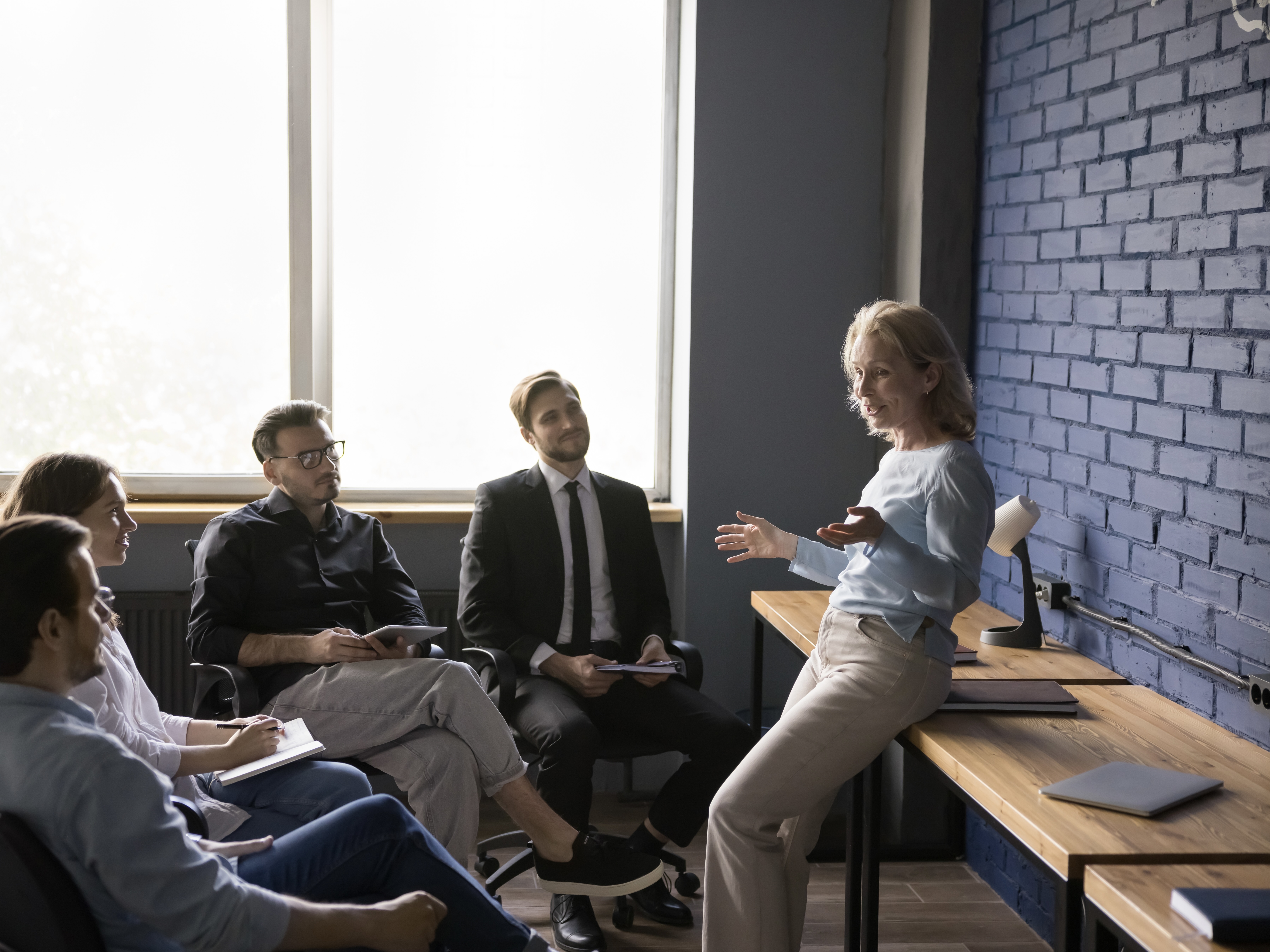  An executive leans on a desk as she speaks to a small group of young professionals.