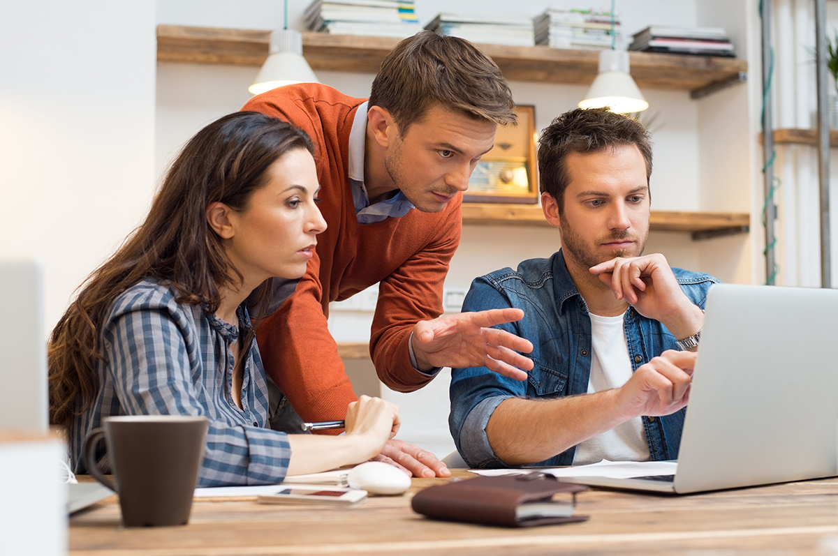 Coworkers having a discussion together while  looking at a laptop in the office