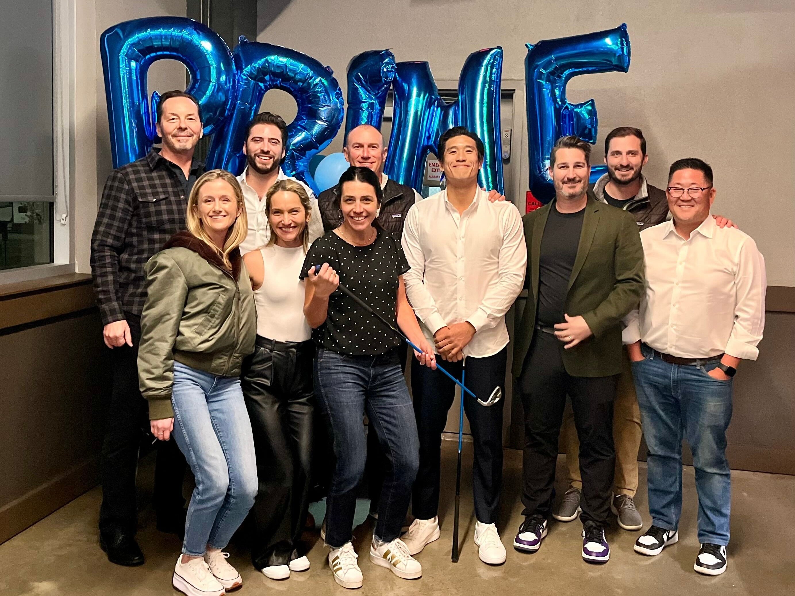 Murphy and the Pinwheel team smile for a group photo in front of inflatable balloon letters spelling out the word Prime.