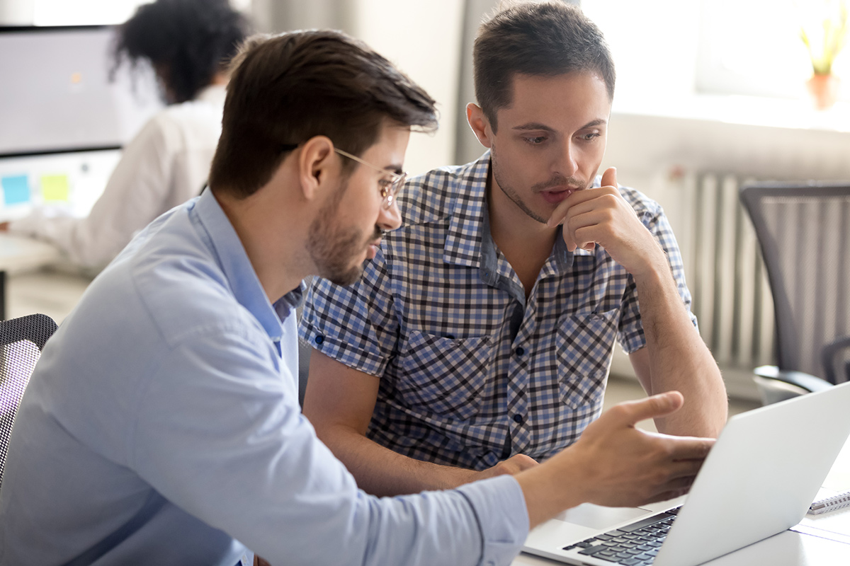 Coworkers working together on project sitting at desk looking at a laptop in an office space