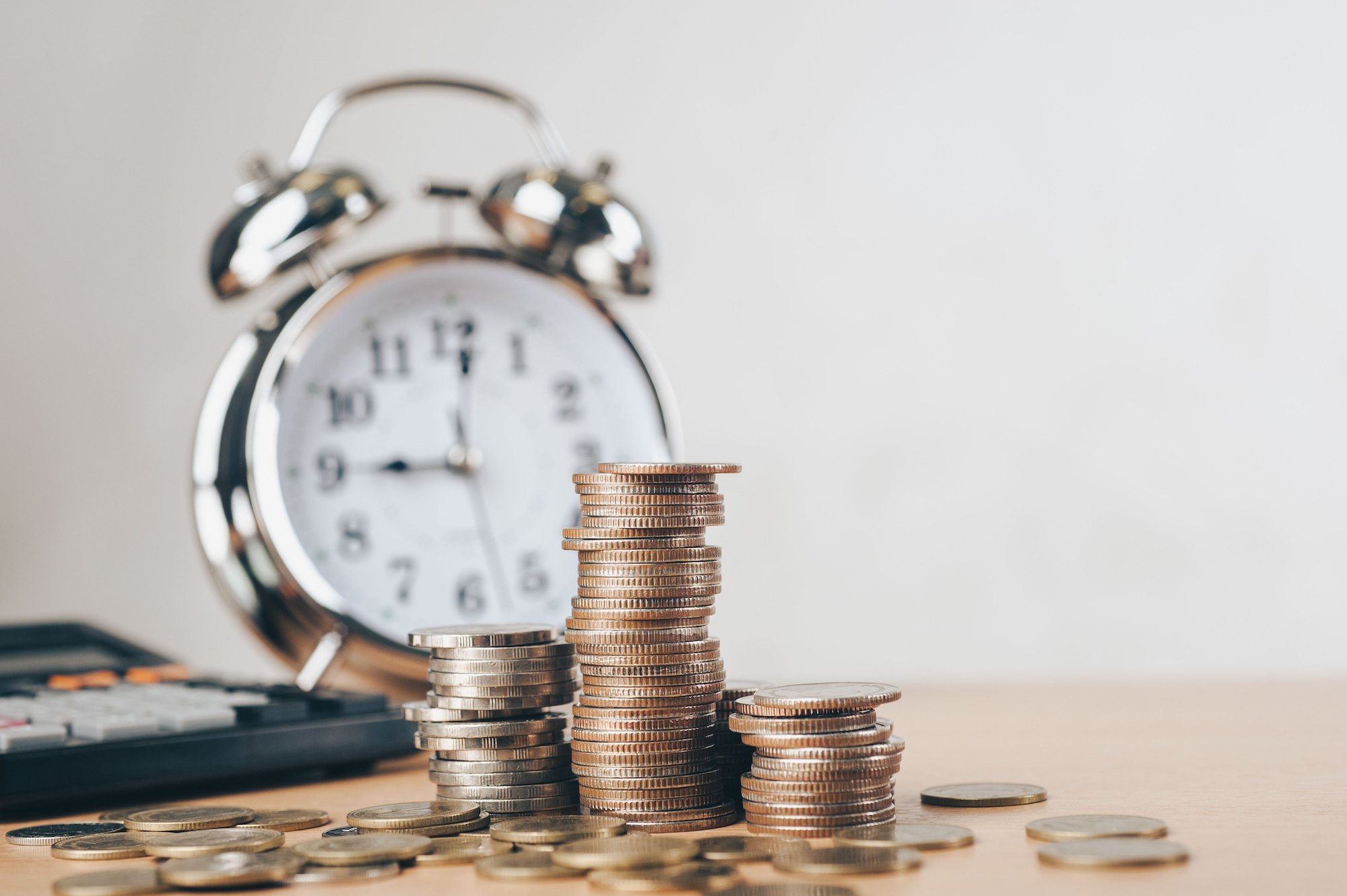 A stack of coins is pictured in front of an alarm clock.