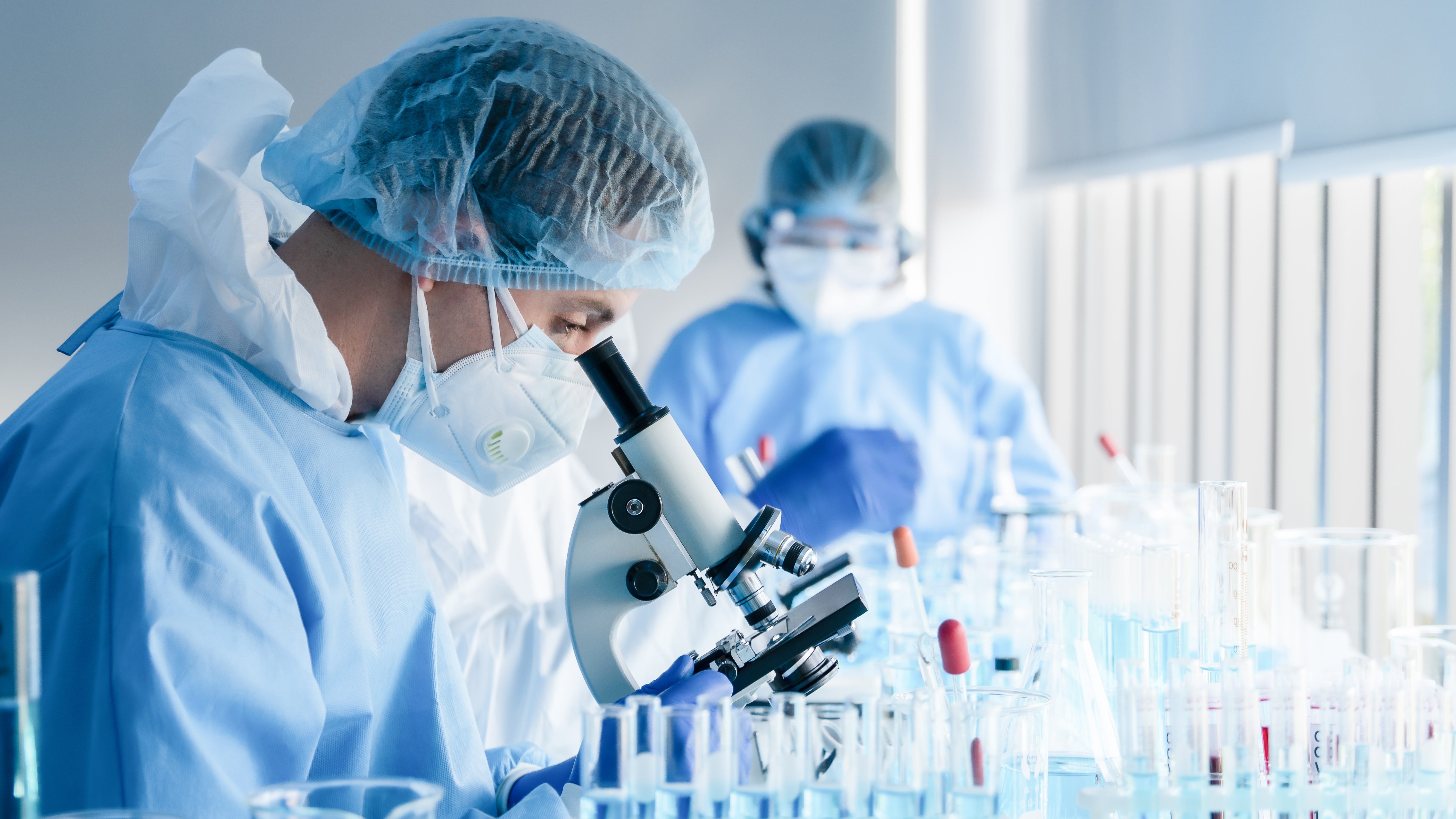 A lab technician in a sterile environment looks into a microscope