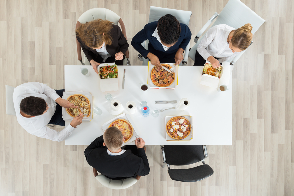 Overhead view of coworkers eating pizzas for lunch together at a table.