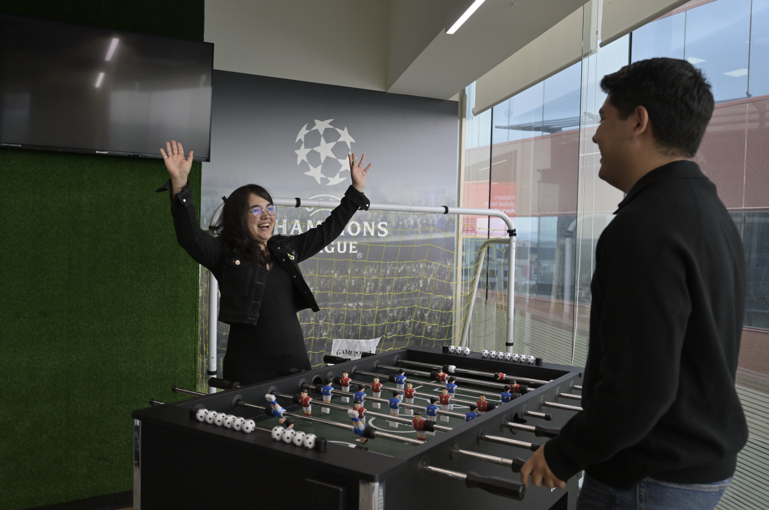 Two WBD colleagues play foosball in front of an image of a professional soccer match.